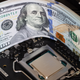 A stack of 100 dollar bills lying next to the uncovered CPU on a computer motherboard.